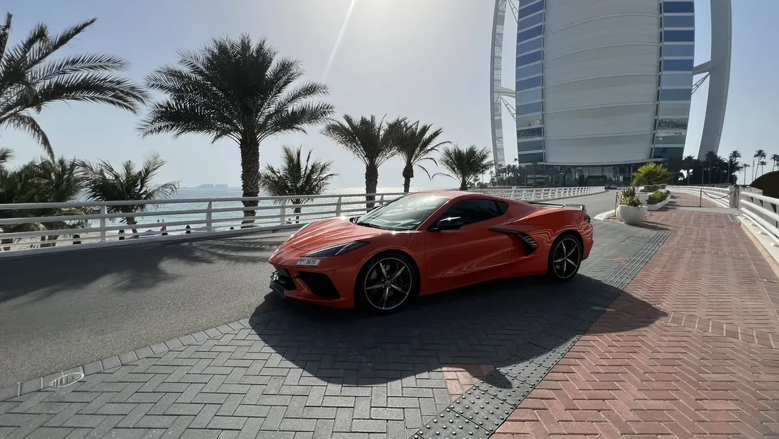Orange Chevrolet Corvette C8 parked on Jumeirah beach road with the Burj Al Arab behind it